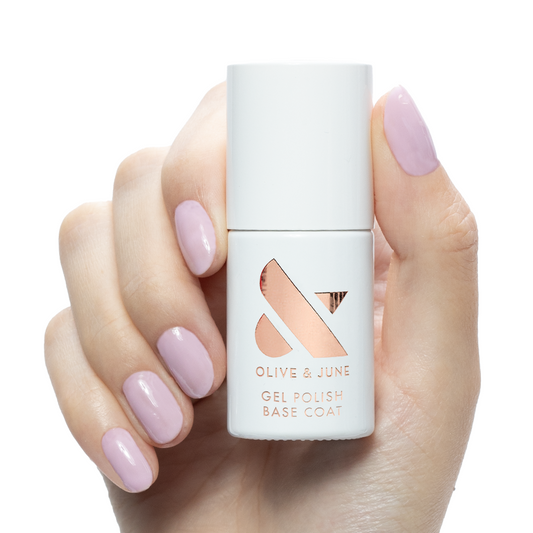 Hand holding Gel Base Coat bottle with soft lavender gel polished nails on white background for manicure prep.