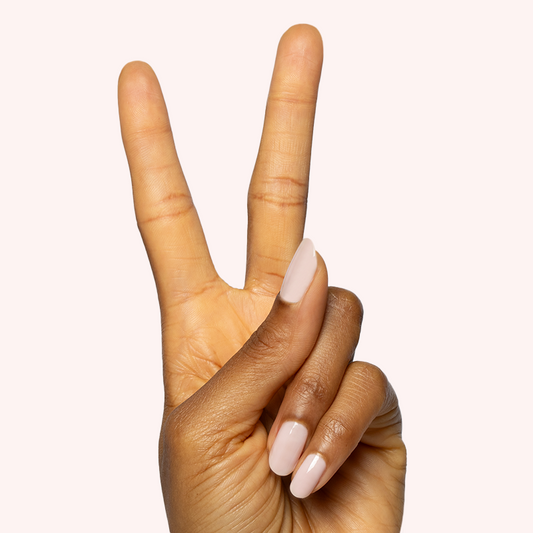 Hand showing two fingers with nails painted in sheer milky pink Puffball gel polish manicure on light background