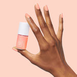 Hand holding Olive and June Wild & Free coral shade polish with matching nails for a bright at-home mani