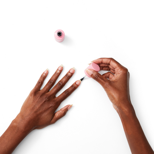 Hand applying Nail Strengthener with brush on natural nails of dark skin tone against white background