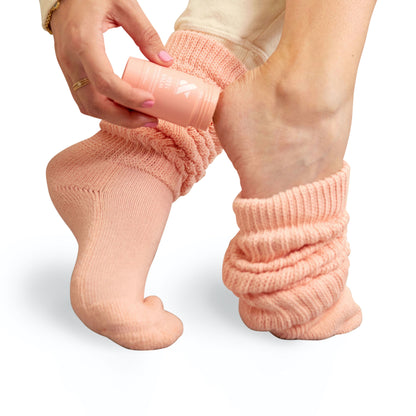 Person applying Overnight Heel Repair Set balm to heel while wearing slouchy peach knit socks on white background