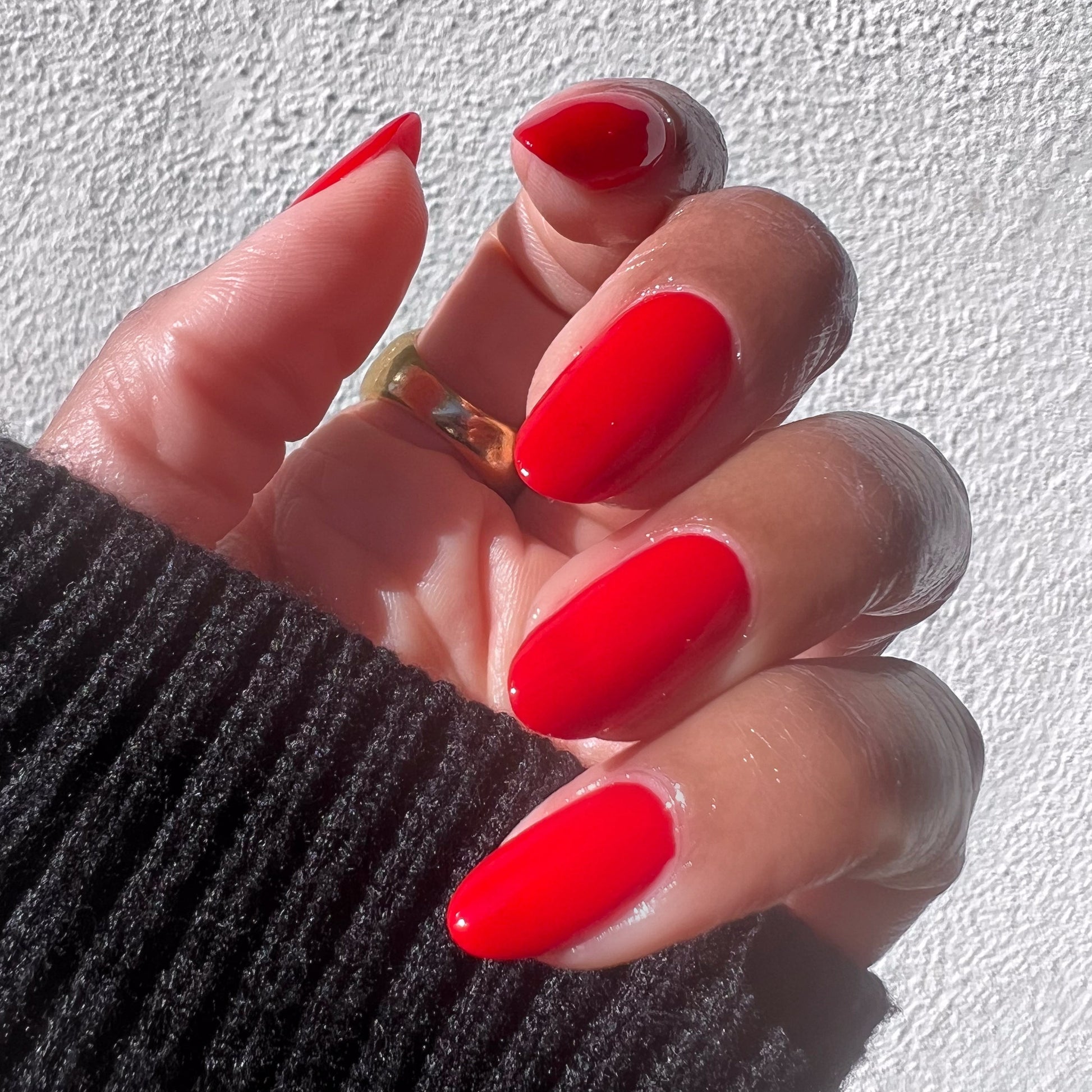 Hand with almond-shaped nails painted in vibrant Lollipop cherry red quick dry polish against textured white background