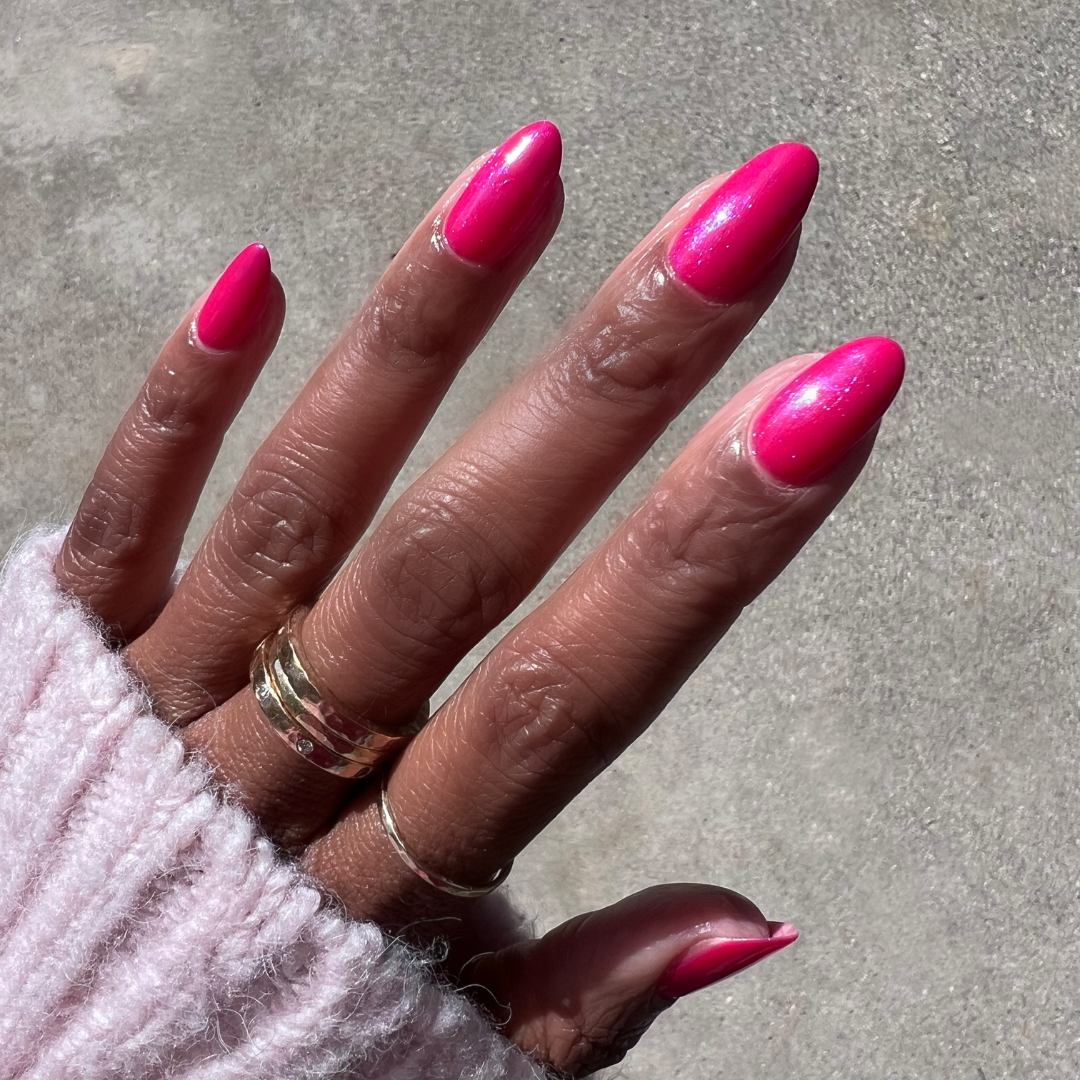 Hand with pointed nails painted in bright pink Berries gel polish showing glossy, long-lasting manicure in sunlight outdoors
