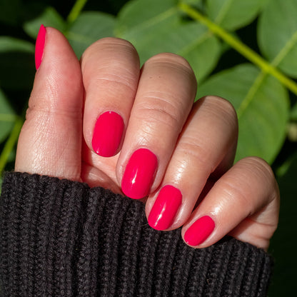 Hand displaying smooth nails painted with XOXO hot pink polish for a bright, long-lasting manicure outdoors