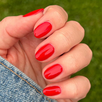 Fingernails painted with glossy Lollipop quick dry polish in bright cherry red against outdoor grass background
