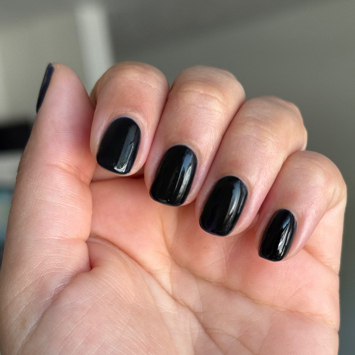 Close-up of hand with short nails painted in glossy black shade using Covet - Gel nail polish for a sleek manicure