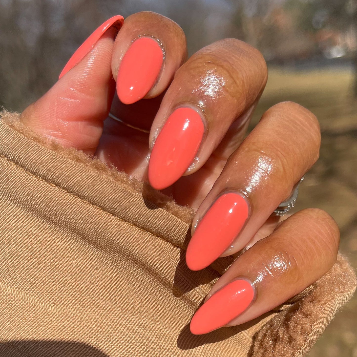Hand with long almond-shaped nails painted glossy Carrot Juice gel polish by Olive and June outdoors in natural light