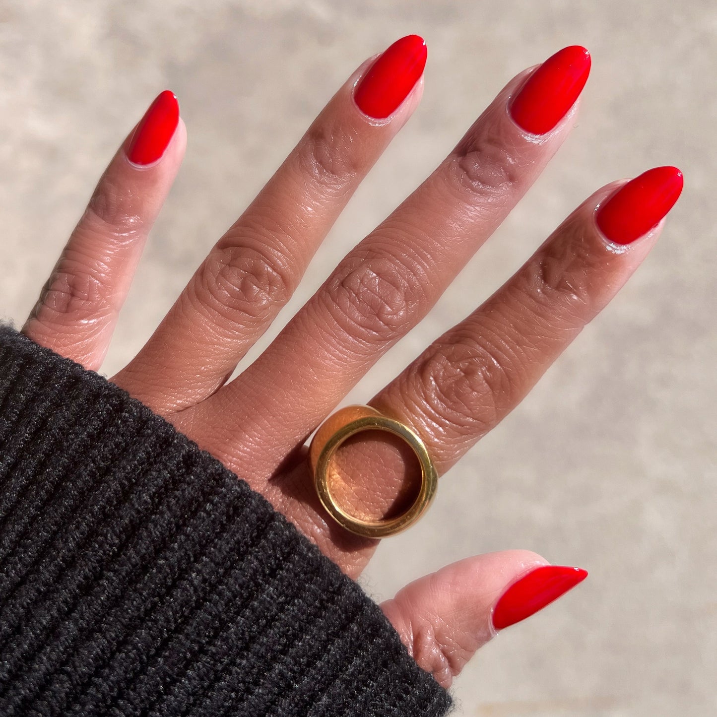 Hand with almond-shaped nails painted in vivid Lollipop quick dry polish wearing bold gold ring on neutral background