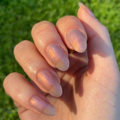 Hand with nails painted in sheer iridescent pink-purple-gold polish Mermaid Hair in sunlight outdoors manicure