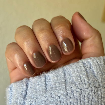Hand with glossy Fawn - Gel polish in a soft minky brown shade, natural nails with cozy light blue sweater sleeve