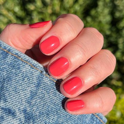 Hand with glossy nails painted in Field Day juicy watermelon red polish holding denim fabric for a fresh mani look