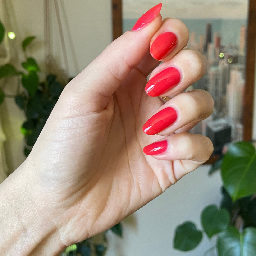 Hand with glossy Fragola nail polish in sheer strawberry pink jelly shade showing smooth manicure indoors