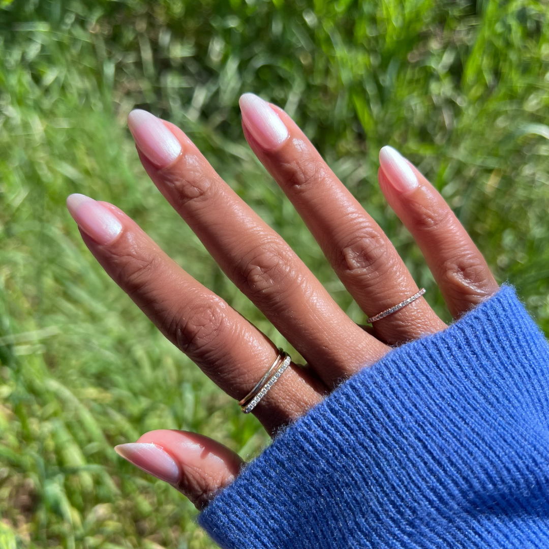 Hand with almond-shaped nails coated in Freshwater sheer pearly polish showing a natural glossy at-home manicure outdoors