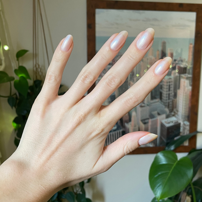 Hand with slender natural nails coated in Freshwater sheer pearly gel polish showing a glossy at-home manicure indoors