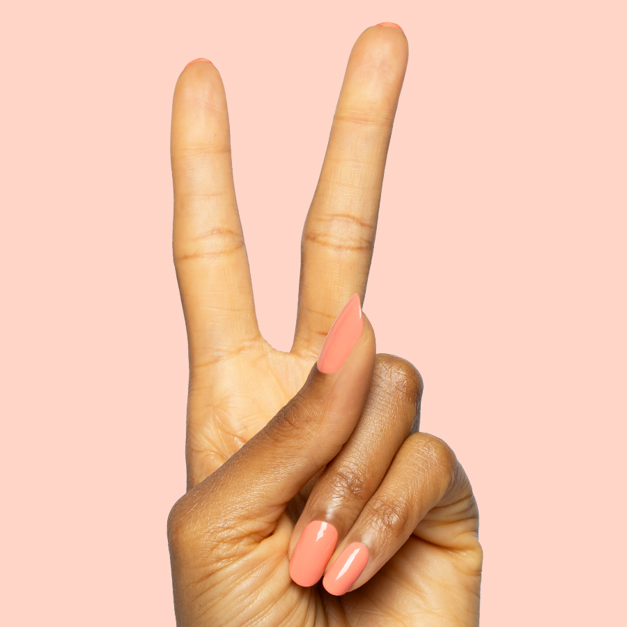 Hand showing peace sign with nails painted in bright orangey coral Frolic quick dry gel polish on soft peach background