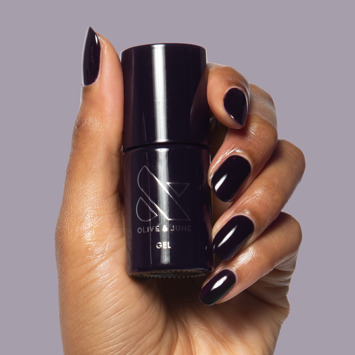 SD - Gel bottle held with matching deep plum gel polish on almond-shaped nails by Olive and June