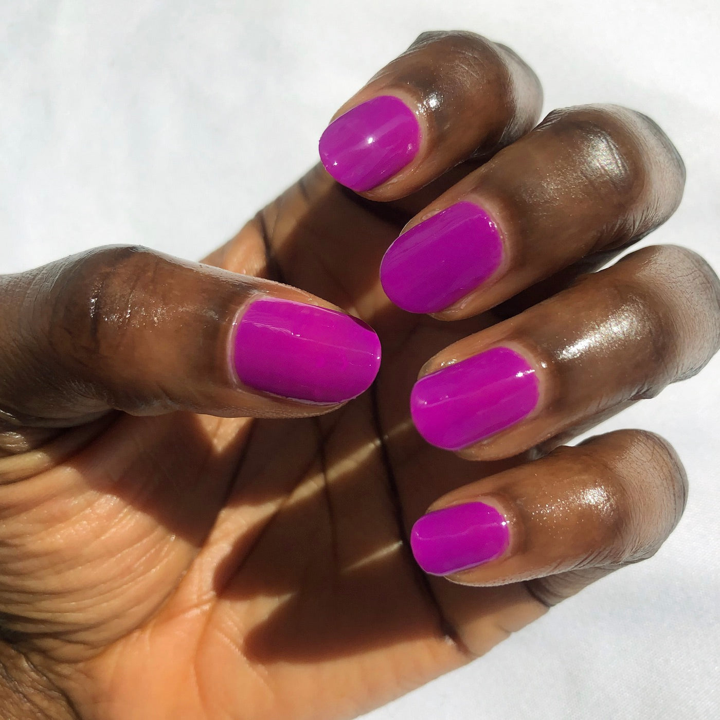 Close-up of hand with nails painted bright purple Grape Soda polish showing glossy manicure in natural light