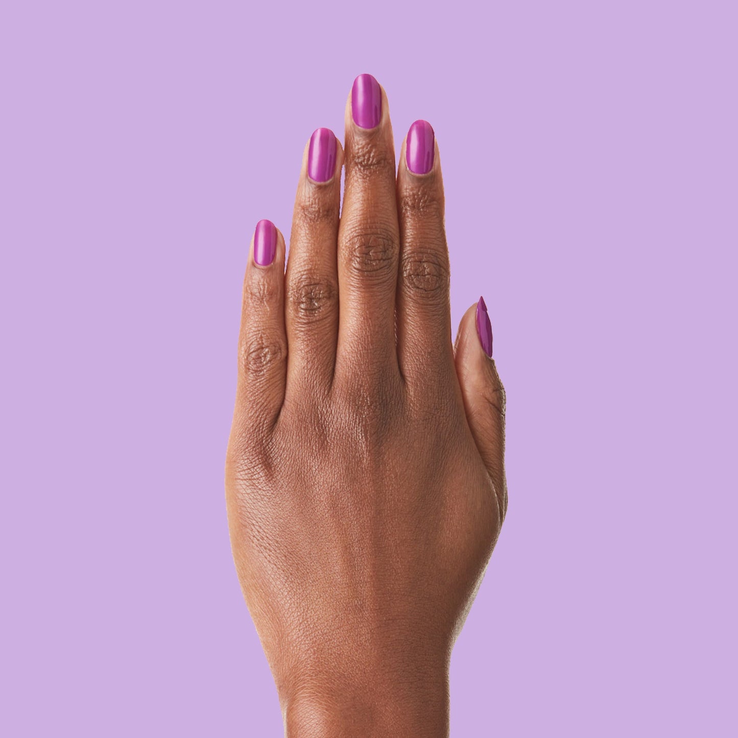 Hand with nails painted bright purple Grape Soda polish showing smooth glossy manicure on lavender background