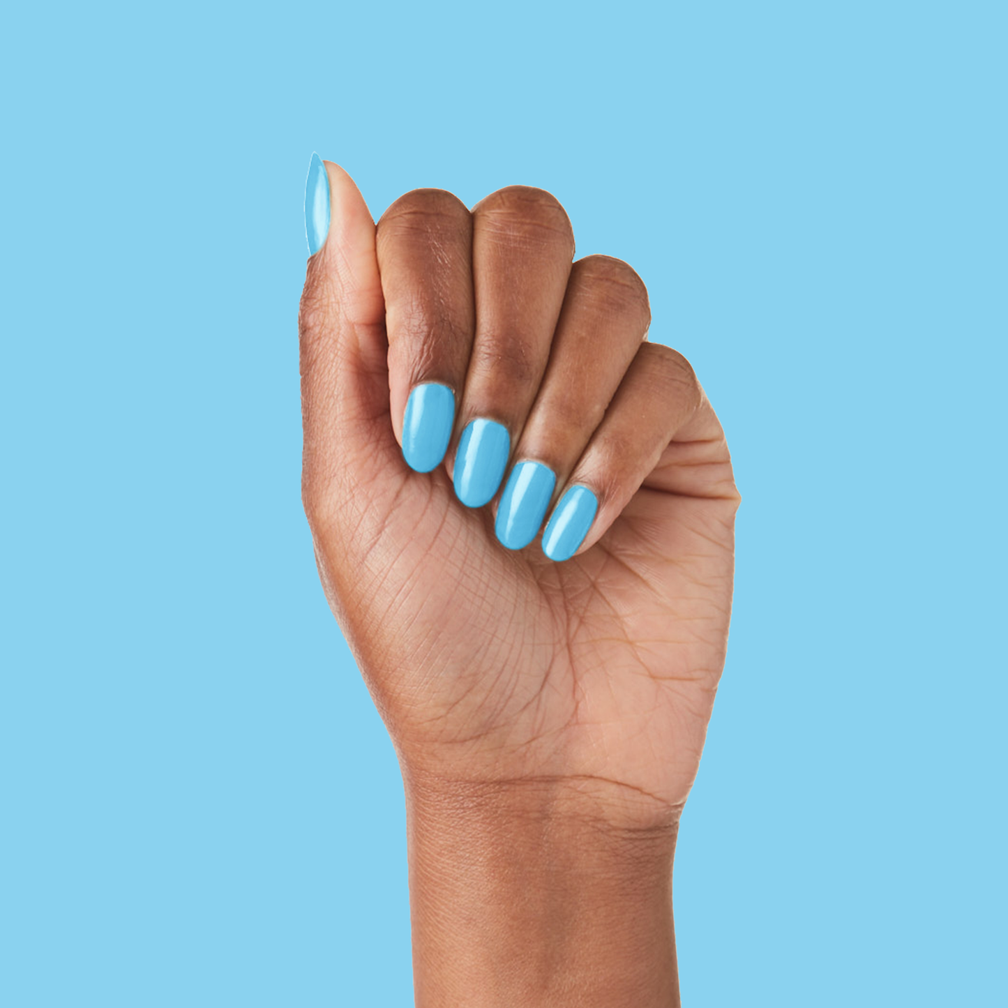 Hand with nails painted in glossy Megababe Blue gel polish against matching blue background for polished mani look