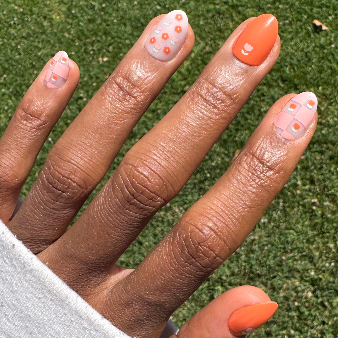 Hand with Mixed Quilt Print - Press-On | Short | Almond nails featuring floral and plaid patterns in soft peach and orange shades for easy mani