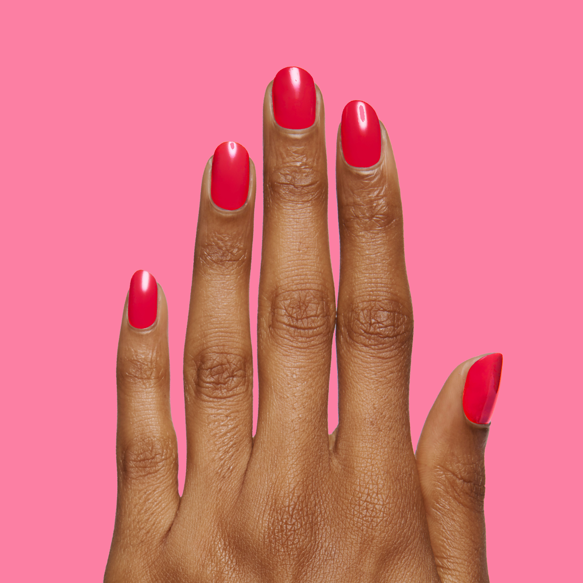 Hand with nails painted in vibrant Hibiscus polish by Olive and June showing bright tropical pink manicure on pink background