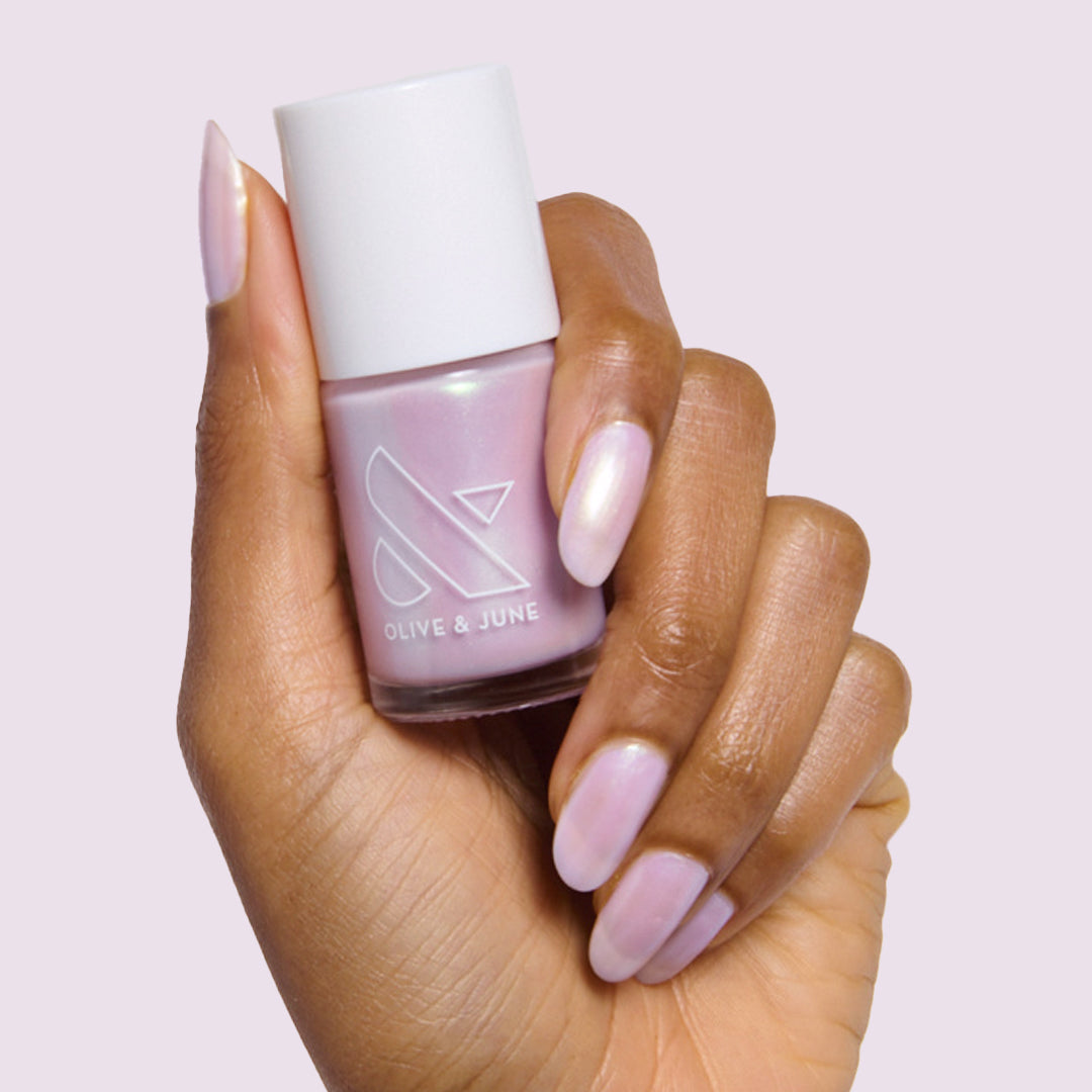 Hand with almond-shaped nails painted in glossy Purple Puka gel polish holding bottle of milky lavender iridescent polish