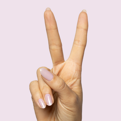 Hand with natural nails painted in sheer milky pastel lavender Dreamy gel polish on soft pink background showing peace sign