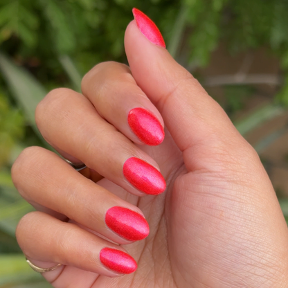 Hand with medium-length nails painted bright pinky-red with silver shimmer using Rodeo Queen polish for a polished mani