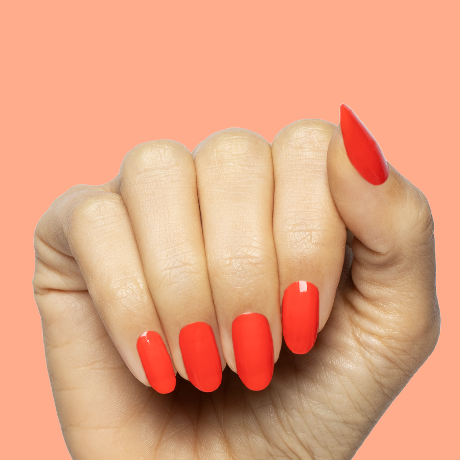 Hand with medium-length nails painted in bright Snapdragon quick dry gel polish on soft coral background