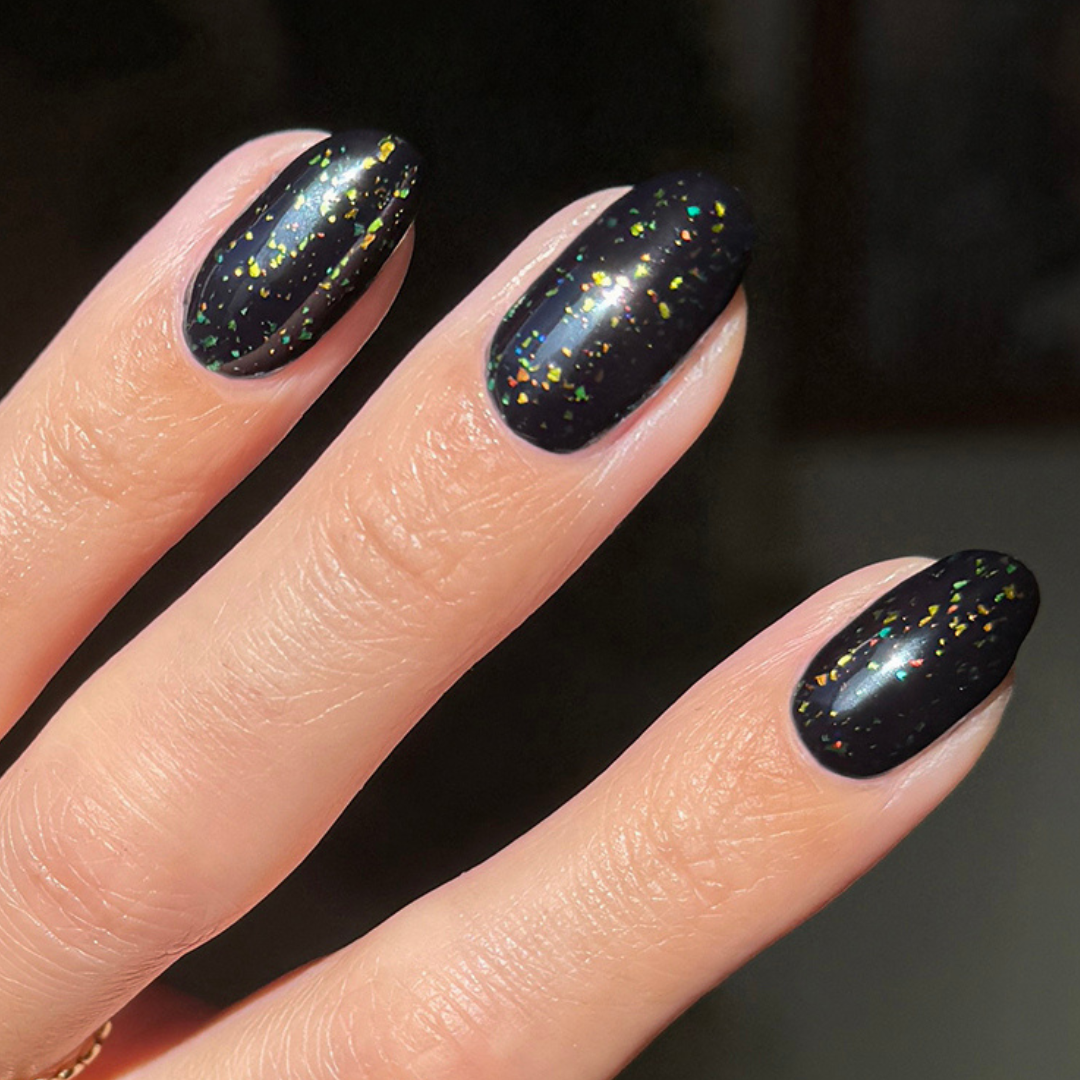 The Stardust Effect Top Coat layered on black polish with multicolored holographic flakes for a shiny mani finish