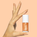 Hand holding a bottle of Sunlit warm golden peach shimmer quick dry gel polish against matching peach background