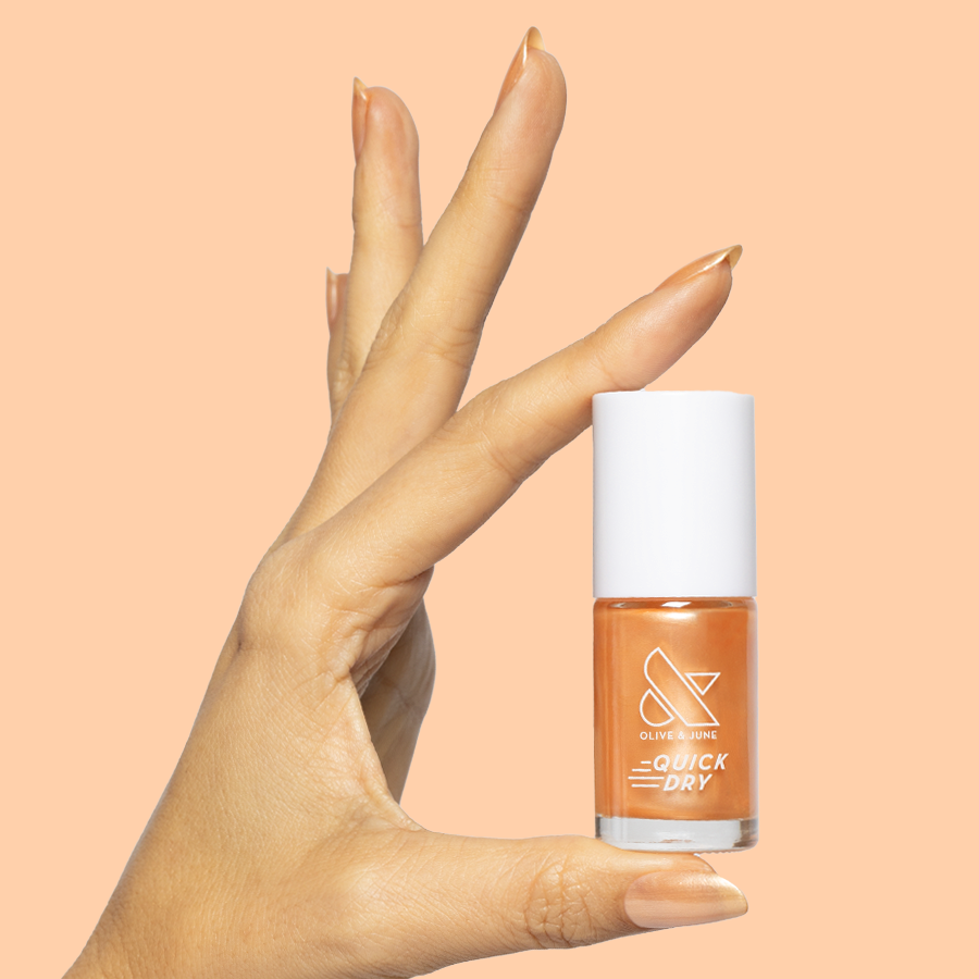 Hand holding a bottle of Sunlit warm golden peach shimmer quick dry gel polish against matching peach background