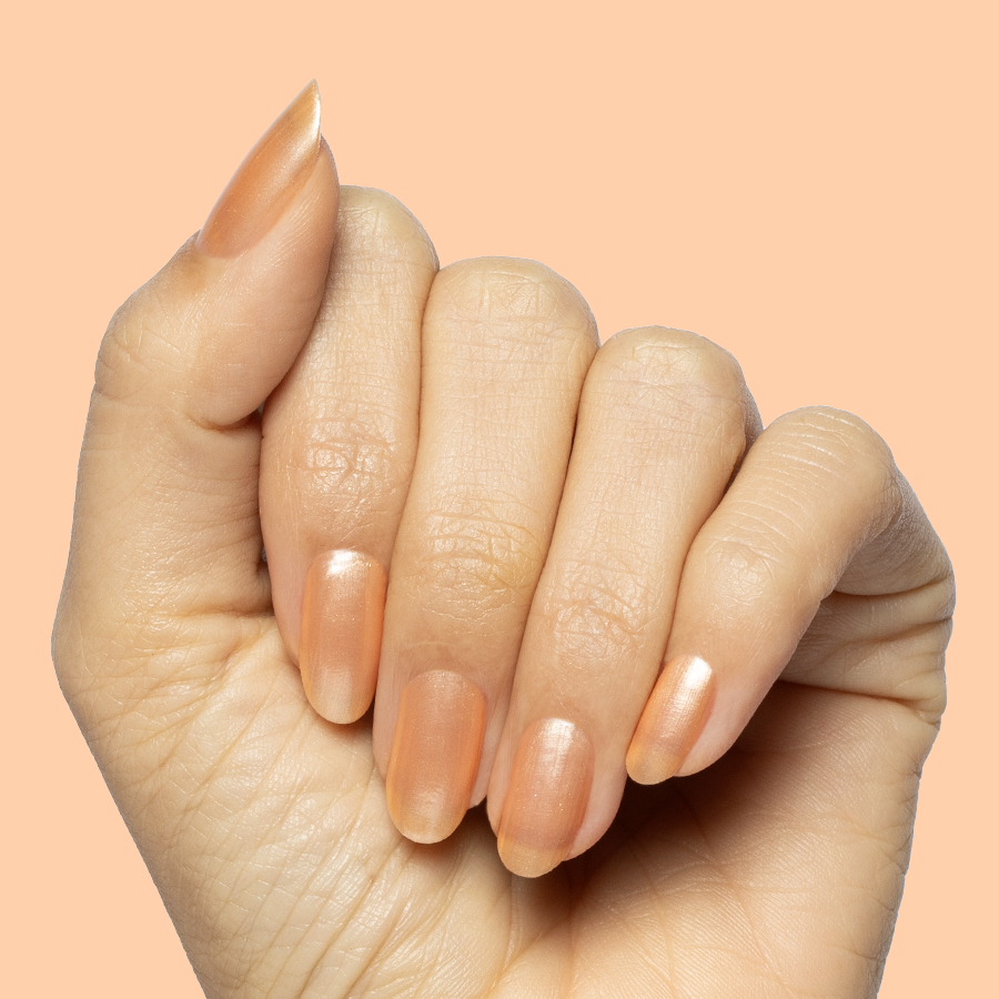 Hand with natural nails coated in Sunlit warm golden peach shimmer gel polish on a soft peach backdrop