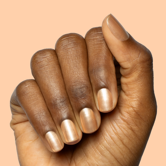 Hand with short rounded nails painted in Sunlit warm golden peach shimmer gel polish on peach background