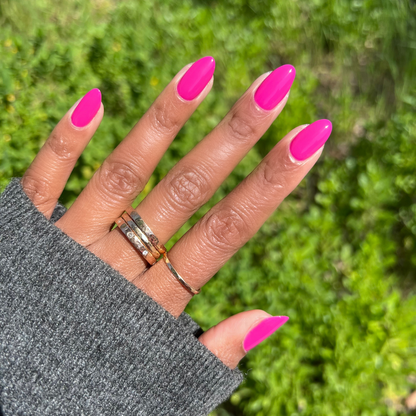 Hand with long almond-shaped nails painted in bright orchid magenta Wildest gel polish against green outdoor background