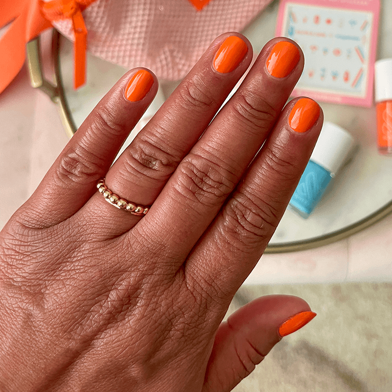 Hand with nails painted in bright tangerine "You're a 10" gel polish showing glossy fresh manicure at home