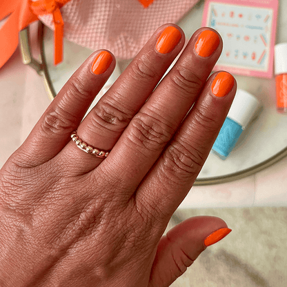 Hand with nails painted in bright tangerine "You're a 10" gel polish showing glossy fresh manicure at home