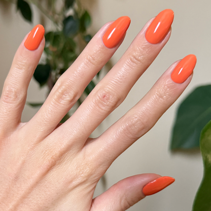 Hand with almond-shaped nails painted bright tangerine orange using Bounce Back quick-dry polish for a polished mani