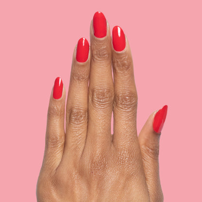 Hand with nails painted in glossy cherry red Lollipop quick dry polish against a soft pink background