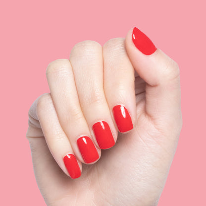 Hand with nails painted in glossy cherry red Lollipop polish against a soft pink background