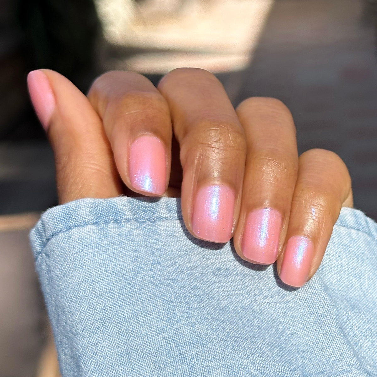 Close-up of hand with short nails painted in sheer iridescent pink-blue Olive Y'all gel polish manicure outdoors